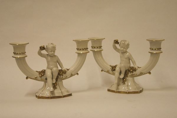 Coppia di candelieri, sec. XX, in porcellana decorata a putti, a due luci, cm 17