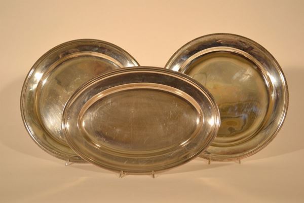 Lottto composto da: coppia di grandi vassoi circolari in rame argentato con tesa rialzata cesellata a palmette,diam. cm 39 e vassoio ovale in metallo argentato liscio, lungh. cm 42, fine sec. XIX (3)
