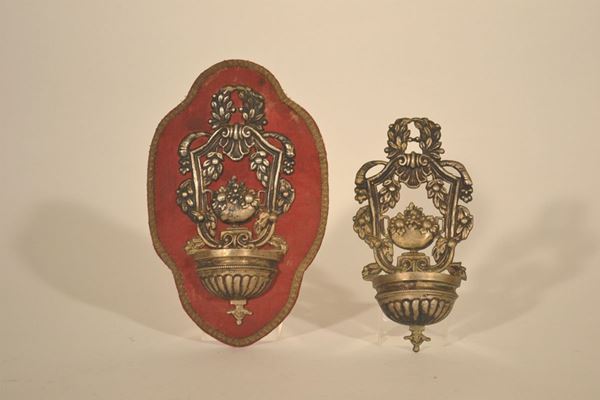 Coppia di acquasantiere in metallo argentato  con vaschetta baccellata e pannello traforato e coppa fiorita, sec. XIX, una applicata su pannello rivestito in stoffa rossa, alt. cm 18 (2)