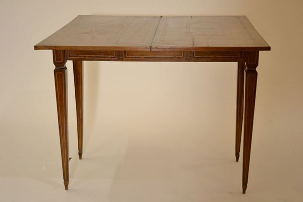 Tavolino da gioco, Rolo, inizi sec. XIX, in noce e radica di noce intarsiato e filettato, piano ad aprirsi a libro decorato d riserve geometriche concentriche centrate da volute vegetali contrapposte, fascia rettilinea, gambe troncopiramidali con collarino su piedi affusolati,chiuso cm 97x48x79 Cfr.: AAVV, L'arte della tarsia a Rolo, Rolo 1996, p. 194-195, nn. 145-148