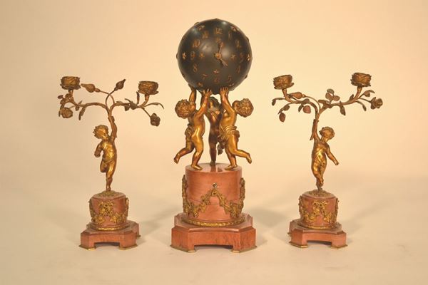 Trittico da camino composto di: orologio e coppia di candelabri rispettivamente realizzati con putti  che sorreggono una cassa sferica ad imitazione del mondo e putti con tralci a due portacandele (3)