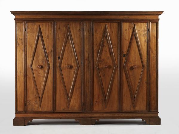 Grande armadio, Italia centrale, inizi sec. XVII, in gattice a patina bionda con profili e cornici in noce, cappello rettilineo con profilomodanato, fronte a quattro sportelli decorati da grandi losanghe che si  ripetono anche sui fianchi e alternati da lesene stilizzate, base modanata, piedi a mensola, cm 295x57x226