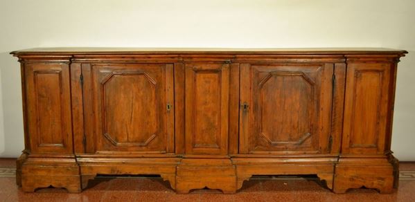 Credenza in stile Seicento, in noce a patina bionda, piano sagomato, frontea due sportelli scorniciati fra lesene stilizzate, base modanata, piedi amensola, cm 252x51x91, costruita con materiale antico