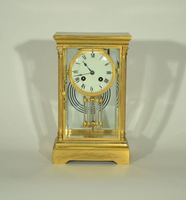 Orologio da tavolo, in bronzo dorato e vetro, cassa rettangolare entro cui si trova il quadrante con numeri romani, fronte inquadrato da colonne scanalate, alt. cm 28