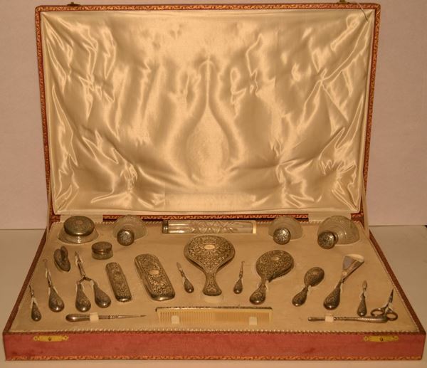 Servito da toilette, sec. XX, in argento cesellato a volute vegetali e cristallo composto di sei tra spazzole e pettini, sei flaconi, due allacciabottoni, un calzascarpe, otto accessori da toilette, entro scatolaoriginale (23)