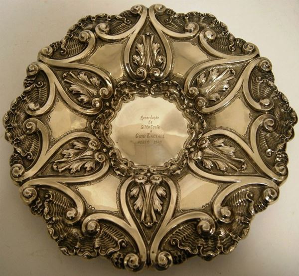 Centrotavola, Portogallo, metÃ  sec. XX, in argento, riccamente sbalzato e lavorato a motivo conchigliforme a volute ed elementi vegetali, al centro incisione con dedica, diam. 37,5, gr. 699