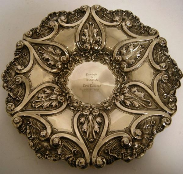 Centrotavola, Portogallo, meta' sec. XX, in argento, riccamente sbalzato e lavorato a motivo conchigliforme, a volute ed elementi vegetali, al centro incisione con dedica, diam. 37,5, gr. 699