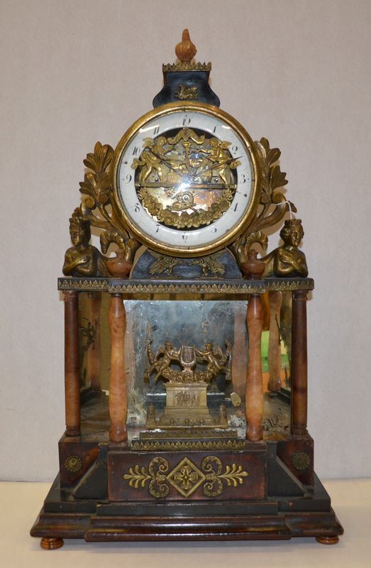 Orologio da tavolo, Austria, sec. XIX, di forma a tempietto in legno e legno ebanizzato, base decorata da guarnizioni in bronzo dorato e cesellato a motivi vegetali, fronte a specchio fra colonne in alabastro su cui poggia il quadrante con numeri arabi centrato da placchetta traforata a putti in bronzo dorato ed affiancato da figure fantastiche realizzate a tutto tondo, alt. cm 68, meccanismo da revisionare