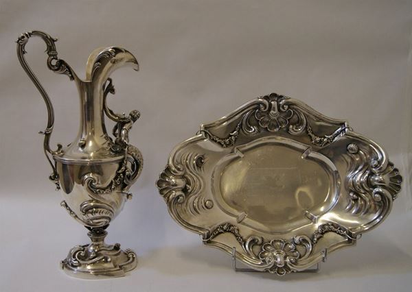 Anfora, in argento, di forma ovoidale, su base sagomata, corpo modellato a volute vegetali, conchiglie e figura di tritone, manico sagomato e becco sbalzato, alt. cm 42, e Vassoio, in argento, dalla tesa sbalzata e riccamente modellata a volute e conchiglie, cm 42x32, complessivi gr. 2650(2)