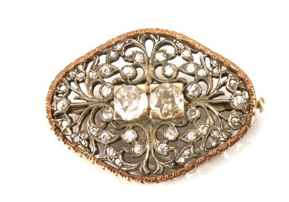 Spilla in oro, argento e diamanti di forma ovale sagomata in argento traforato a volute e punteggiato di diamanti di taglio vecchio, al centro due diamanti di taglio vecchio di ct  0,80 circa ciascuno,. bordo e fodera in oro, g 12