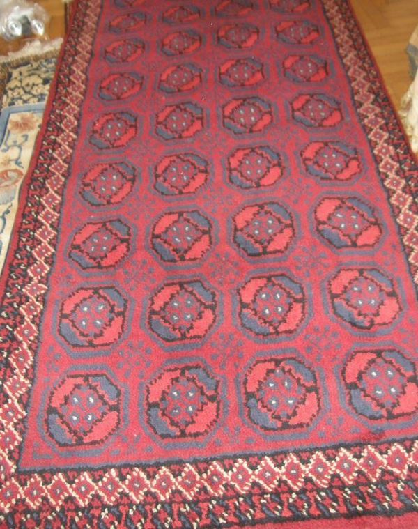 Tappeto fondo rosso, campo decorato a motivi ottagonali nei toni del        celeste e del rosso, bordura a losanghe in avorio, cm 117x245