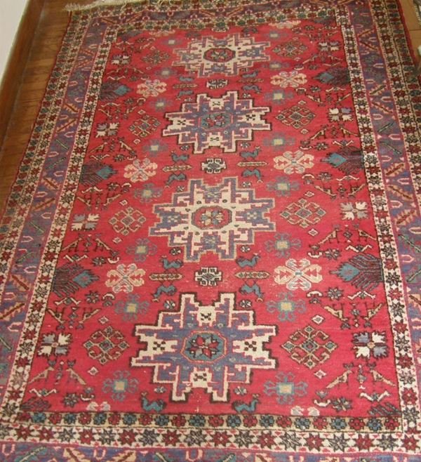Tappeto fondo rosso, al centro quattro elementi a stella nei toni           dell'avorio e del violetto, bordura a motivi geometrici in avorio, violetto e verde olio, cm 139x223