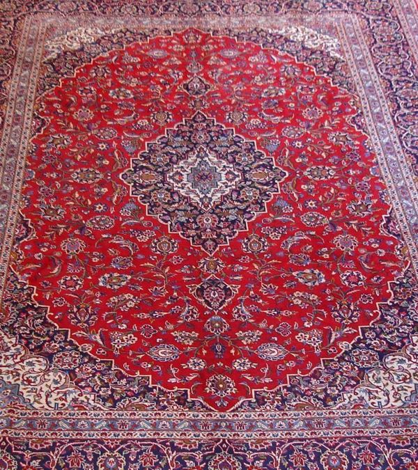 Tappeto persiano Keishan, di vecchia manifattura, firmato, fondo rosso, campo a motivo floreale multicolore, con medaglione centrale e bordura blu, cm 405x290