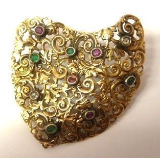Spilla in oro giallo, rubini, smeraldi e rose di diamante                   di forma sagomata in oro giallo traforato e cesellato a volute impreziosite da piccoli rubini, smeraldi e rose di diamante montati entro castoni ovali e circolari a colletto, g 14