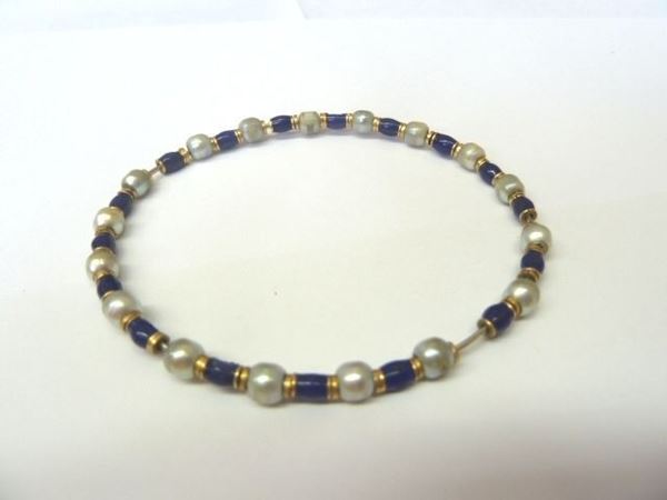 Bracciale in oro, smalto e perle                                            realizzato a cerchio rigido, formato da una fila di piccole perle di fiume  intercalate da piccoli anelli in oro ed elementi cilindrici decorati in     smalto blu, anima in metallo