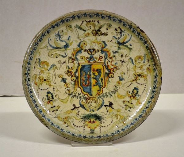 Piatto, sec. XVII, in maiolica fondo bianco interamente decorato a putti    musicanti e cupidi tra raffaellesche, al centro stemma araldico, diam. cm   24,5, reca sul retro etichetta in carta Ongaro AntichitÃ  Milano, lievi      danni