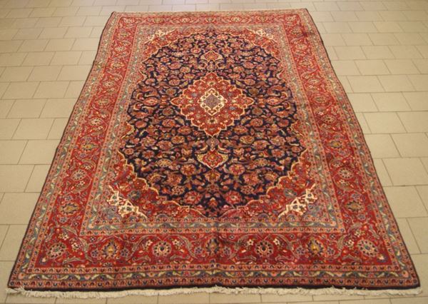 Tappeto persiano keishan, di vecchia manifattura, fondo blu, campo a motivo floreale, con medaglione centrale e bordura rossa, cm 395x255