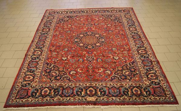 Tappeto persiano kashmar, firmato e di vecchia manifattura, fondo rosso, campo a motivo floreale multicolore, con medaglione centrale e bordura blu, cm 400x297