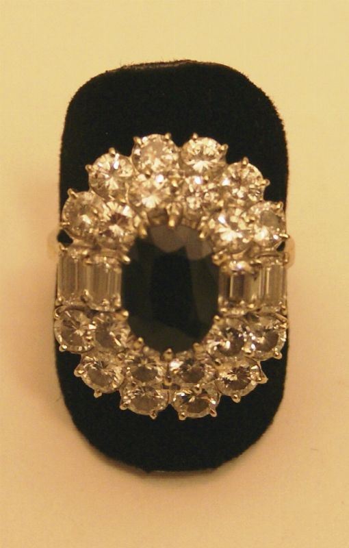 Anello, in oro bianco, con zaffiro ovale scuro al centro, montato entro cornice in brillante e diamanti baguette, gr. 6,7