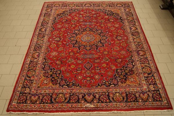 Tappeto persiano kashmar, firmato, di vecchia manifattura, fondo rosso, a motivo floreale, con medaglione centrale e bordura blu, celeste e arancione, cm 405x290