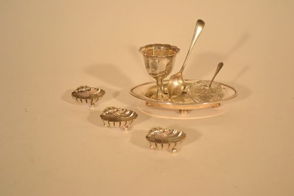 Lotto composto da: tre piccole saliere in argento in forma di conchiglia su tre piedini sferici, una con cucchiaino, portauovo con cucchiaio in metallo argentato, vassoietto ovale e saliera vetro, sec.XX (7)