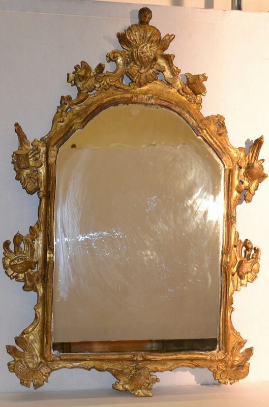 Piccola specchiera, Veneto, sec. XVIII, in legno intagliato e dorato,       sormontata da busto maschile panneggiato e decorata a motivi di gusto       rocaille arricchiti da panoplie di armi, cm 107x71, specchio di epoca       posteriore, alcuni danni