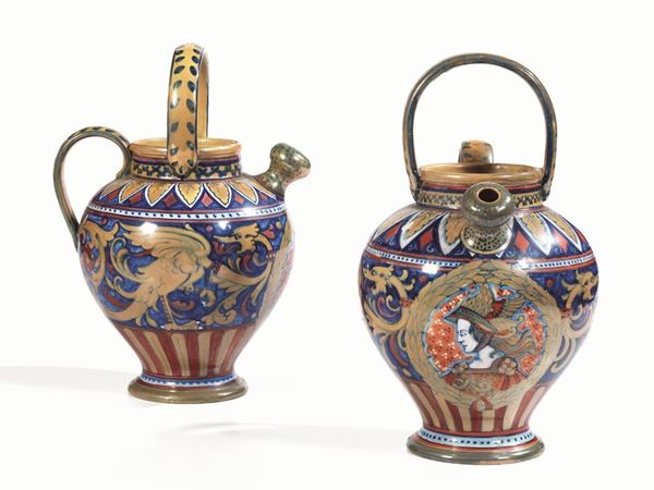 Coppia di brocche, manifattura Rubboli,  Gualdo Tadino, inizi sec. XX, di   forma globulare, in                                                         maiolica a lustro metallico decorata ad animali fantastici nei toni del     blu, oro e rosso, anse a nastro e presa superiore a semicerchio, alt. cm    34, recano il marchio alla base, una lieve sbocconcellatura alla base di    una brocca (2)