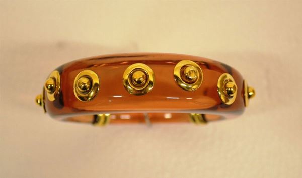 Bracciale in acrilico e argento dorato                                      realizzato come a cerchio rigido bombato color ambra con guarnizioni        circolari e chiusura in argento dorato
