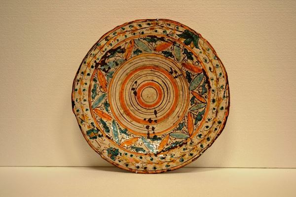 Piatto in maiolica di gusto arcaico decorato nei                            toni del verde rame, giallo senape e bruno