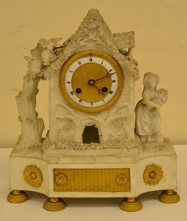 Orologio,  fine sec. XVIII- inizi XIX, in bisquit e bronzo dorato, modellato a casetta campestre centrata da quadrante circolare, base decorata in bronzo,  mancante del pendolo, lievi danni