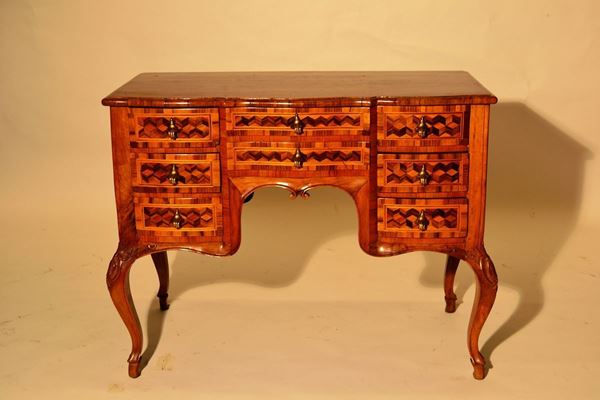 Scrivania, in stile Settecento, in noce a patina bionda, fronte mosso a otto cassetti intarsiati a marqueterie, gambe sinuose, cm 99x52x79