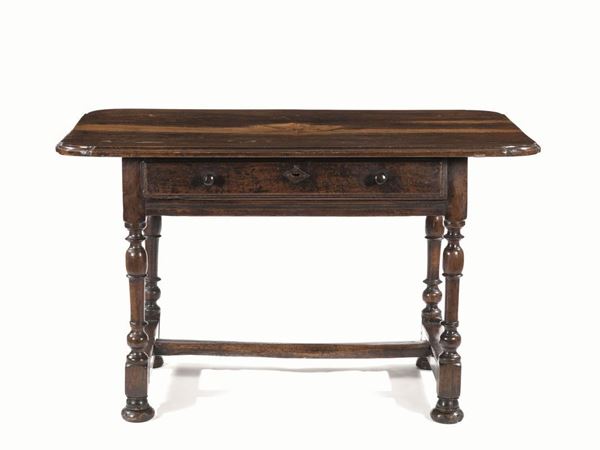 Tavolo, Emilia, secolo XVII, in noce intagliato a patina scura, piano       rettangolare con angoli sagomati, un cassetto nella fascia, gambe tornite a balaustro riunite da traverse su piedi a cipolla schiacciata, cm 129x84x79, alcuni restauri e piano non pertinente