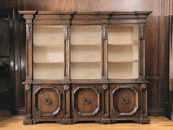 Libreria, in stile Seicento,  in noce a patina scura intagliato con         applicazioni in legno intagliato e dorato, cappello modanato, tre vani a    giorno intercalati da lesene, parte inferiore a tre sportelli con formelle  sagomate, base modanata, piedi a mensola, cm 266x41x234