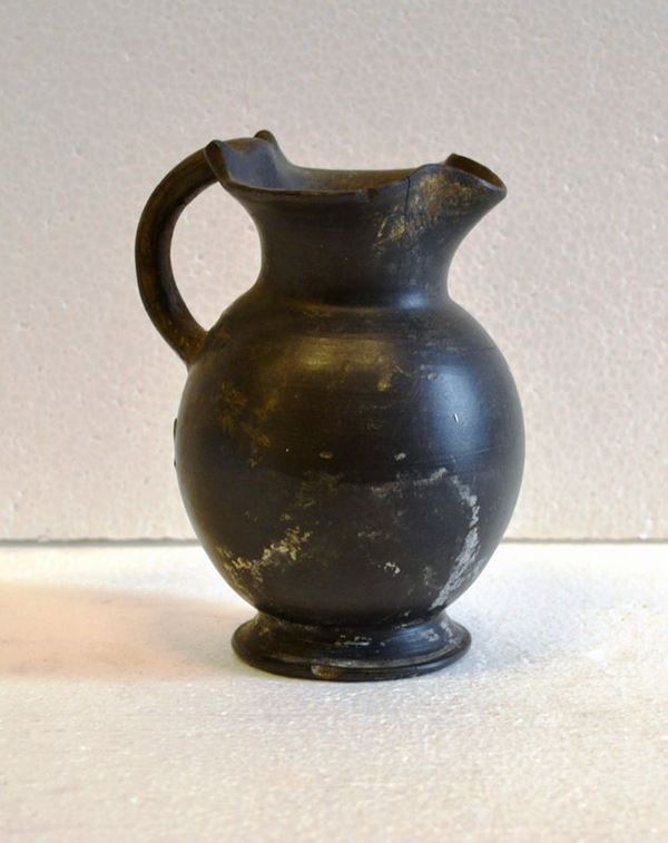 Piccola oinochoe in bucchero                                                Tipo Rasmussen 1979, 7g                                                     Materia e tecnica: bucchero nero lucidato a stecca, modellata a tornio      veloce                                                                      Bocca trilobata, orlo leggermente estroflesso, collo cilindrico svasato in  alto, distinto da un collarino in rilievo, corpo ovoide, basso piede        troncoconico, ansa a nastro impostata sul labbro e sulla spalla con due     piccoli apici nel punto dattacco superiore                                  Produzione: Etruria centro meridionale                                      Stato di conservazione: integra                                             Dimensioni: alt. cm 15, diam. cm 10,5                                       Datazione: II metÃ  VII sec. a.C.                                            Cfr.:G. Rasmussen  Bucchero Pottery in Southern Etruria, Cambridge 1979
