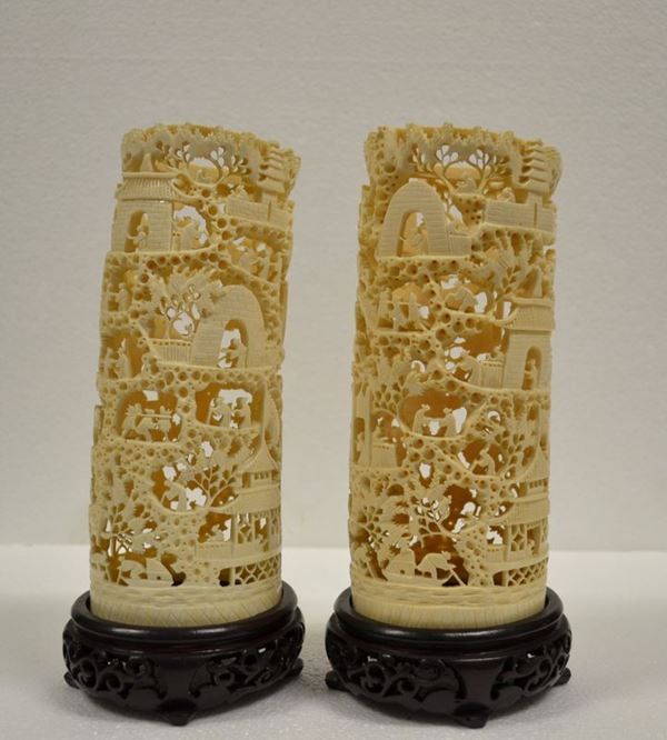 Coppia di intagli Cina sec. XX, in avorio ricavati da porzione di zanna,    lavorati al traforo e raffiguranti personaggi in un paesaggio, alt. cm 21   su basi in legno alt. cm 4,5 (2)