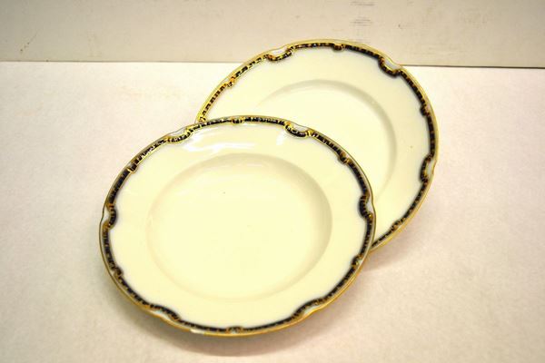 Servito di piatti, manifattura Richard Ginori, in porcellana bianca con tese decorate  da nastro blu-oro, composto di ottantacinque pezzi, danni e sbocconcellature ( 85 ) Composizione: 12 piatti fondi, 34 piatti piani, 11 piattini, 1 insalatiera, 1 zuppiera, 2 alzate, 2 raviere, 2 mostardiere, 1 salsiera, 4 vassoi ovali, 2 vassoi tondi, 13 portauovo