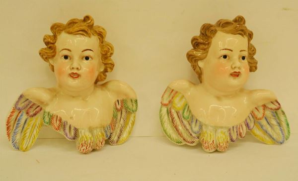 Coppia di busti, sec. XX, raffiguranti putti alati, in ceramica policroma, cm 16x15