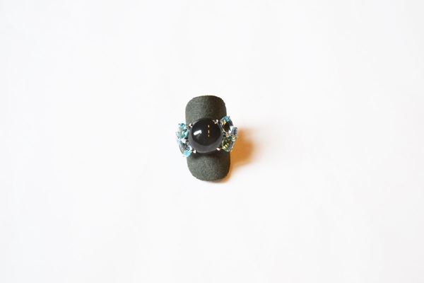 Anello in oro bianco, pietra di luna, topazi e diamanti. Al centro una pietra di luna cabochon affiancata su due lati da tre topazi in varie tonalitÃ  dell'azzurro, di taglio a goccia e brillante e piccoli brillanti, misura 13-14