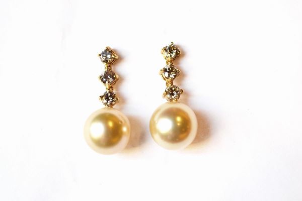 Paio di orecchini pendenti in oro giallo, perle e diamanti, ciascuno realizzato con una linea di tre brillanti montati entro castoni a griffe a cui Ã¨ sospesa un perla South Sea diam. mm 10,5
