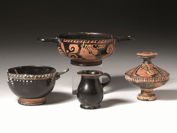 Skyphos nello stile di Gnathia, olpe miniaturistica a vernice nera, coppetta daunia monoansata ed un unguentario fusiforme    Materia e tecnica: argilla figulina rosata, vernice nera lucente,  suddipinture a vernice bianca, modellati a tornio veloce  Skyphos con vasca emisferica, piede troncoconico, anse a bastoncello  impostate obliquamente sotto il bordo, decorato con kyma di ovoli, tralcio con pampini e grappoli stilizzati su entrambi i lati; olpe con corpo ovoide e piede ad troncoconico, coppetta con vasca troncoconica, ansa a nastro  impostata obliquamente, unguentario fusiforme con collo e bocca verniciati in rosso   Produzione: ceramica apula    Stato di conservazione: skyphos mancante di unâ€™ansa e altra ansa lacunosa; olpe integra, coppa integra, unguentario integro incrostato   Dimensioni: alt. da cm 18 a cm 4,8  Datazione: IV-I sec. a.C.