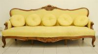 Grande divano, fine sec. XIX, in noce intagliato a patina bionda, spalliera sagomata e centrata da motivo floreale, fascia mossa decorata in maniera analoga, imbottito in cotone operato giallo oro, cm 230x80x105