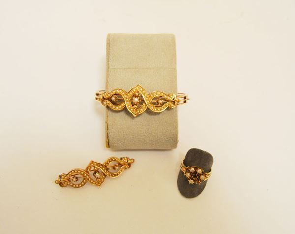 Parure in oro rosa a basso titolo  e microperle composta di bracciale, spilla e anello, Il bracciale a cerchio rigido e la spilla a barretta analogamente decorati da un motivo a nastri intrecciati decorato in microperle, l'anello decorato da piccole perle disposte a formare una corolla, g 30, mancanze(3)