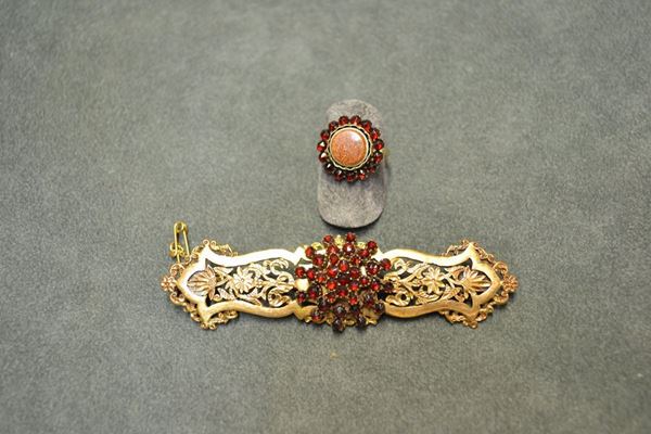 Demi-parure, fine sec. XIX, composta da spilla e anello in oro a basso titolo, granati e avventurina la spilla realizzata come una barretta sagomata traforata a motivi floreali cesellati, al centro corolla formata da piccoli granati; l'anello centrato da un vetro avventurina circolare montato entro una cornice di granati, g 20