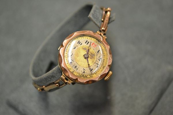 Orologio da polso per signora, inizi sec. XX, in oro rosso a basso titolo Cassa in oro liscio con lunetta sagomata, fondello a scatto. Quadrante bicolore argentÃ¨ e champagne, numeri arabi neri e rosso, lancette traforate. Movimento a carica manuale. Bracciale realizzato ad una fila di maglie a a barretta in oro rosa. Diam. mm 26