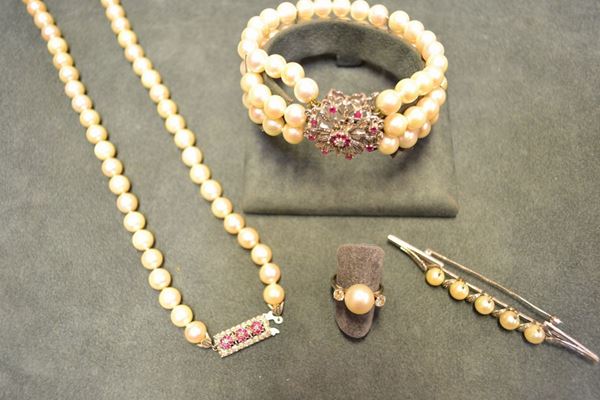 Parure in oro bianco 18 kt e a basso titolo, perle, diamanti e rubini composta di collana, bracciale, spilla e anello la collana realizzata ad una fila di perle diam. da mm 7 a mm 8 con fermatura rettangolare decorata in rubini e brillanti; il bracciale a tre file di perle diam. mm 7, fermatura a fiore in rubini e brillanti; la spilla disegnata come una barretta decorata da perle e piccolissimi brillanti; l'anello con perla centrale affiancato da due brillanti, peso complessivo g 103
