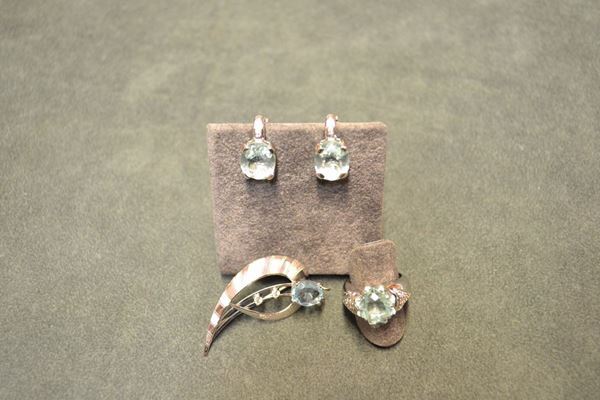 Parure in oro bianco, acquamarina e diamanti, composta di paio di orecchini, spilla e anello paio di orecchini ciascuno realizzato con acquamarina centrale ovale e brillanti; la spilla modellata a forma fantasia con acquamarina ovale e brillanti; l'anello con acquamarina centrale sfaccettata a otto punte affiancata da piccoli brillanti, peso complessivo, g 24