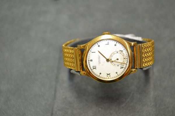 Orologio da polso  Hausmann & Co. Movado, anni '50, in oro giallo 18 kt Cassa con fondello a scatto, lunetta liscia. Quadrante argentÃ¨ con con numeri romani ed indici geometrici smaltati oro, secondi ad ore 6, lancette ad ago. Movimento a carica manuale Movado cal. 75. Bracciale a nastro a maglia tessuto in oro giallo 18 kt non pertinente. Diam. mm 32