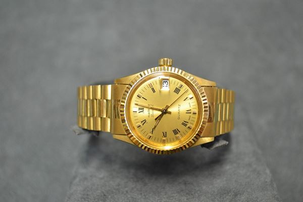 Orologio da polso Daniel, in oro giallo 18 kt Cassa in tre corpi con fondello e coron a vite, lunetta zigrinata, vetro plastica. Quadrante champagne con indici applicati e numeri romani, lancette a bastone, datario ad ore 3, secondi al centro. Movimento al quarzo. Bracciale a maglie in oro giallo, chiusura deployante. Diam. mm 30
