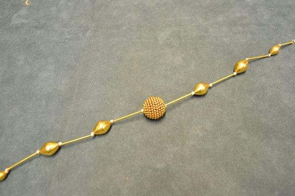 Collana in oro giallo realizzata ad una fila di elementi romboidali in oro, intercalati da bastoncini, al centro una sfera in perline dorate, punzone 750, g 31