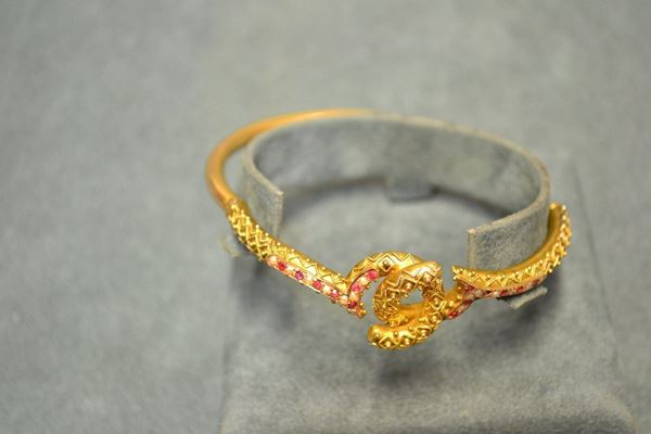 Bracciale, fine sec. XIX, in oro a basso titolo, rubini e microperle modellato a cerchio rigido, la parte superiore con motivo a doppio anello intrecciato lavorato in filigrana e decorato in rubini e microperle, g 11